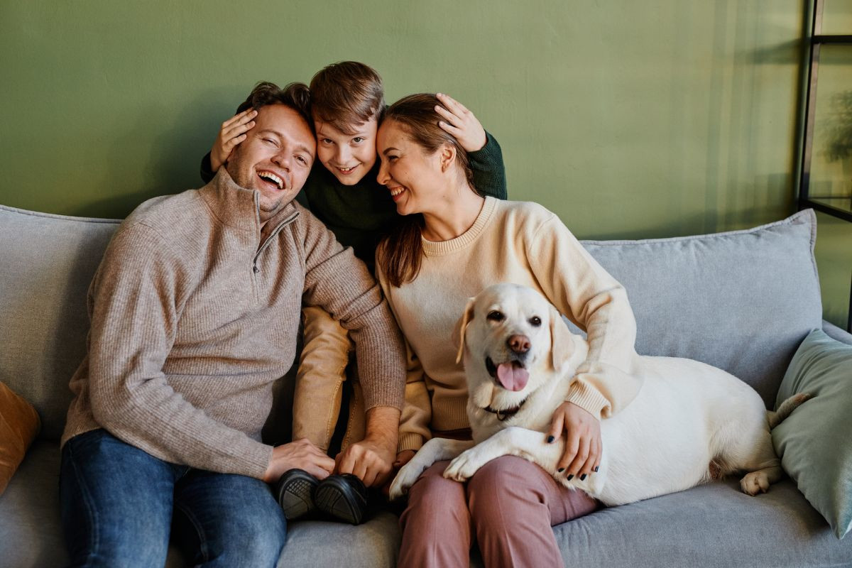 Mom, dad, son and dog sit on a couch enjoying home comfort and smiling at each other