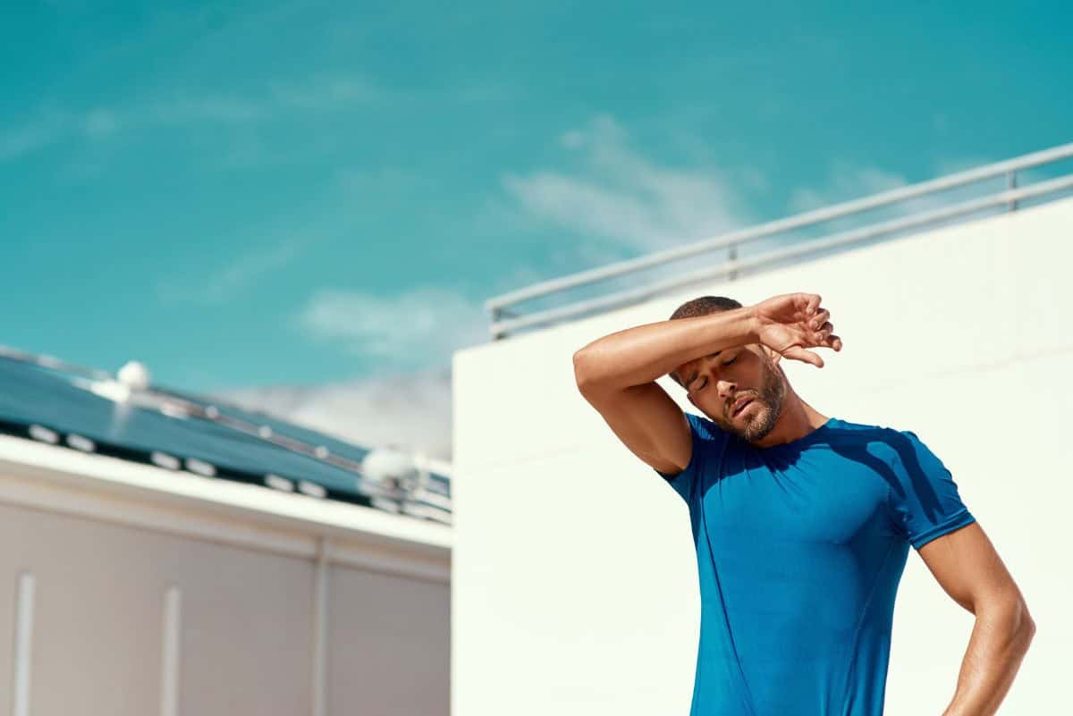 A man wipes sweat from his forehead while exercising outdoors in the Oklahoma heat.