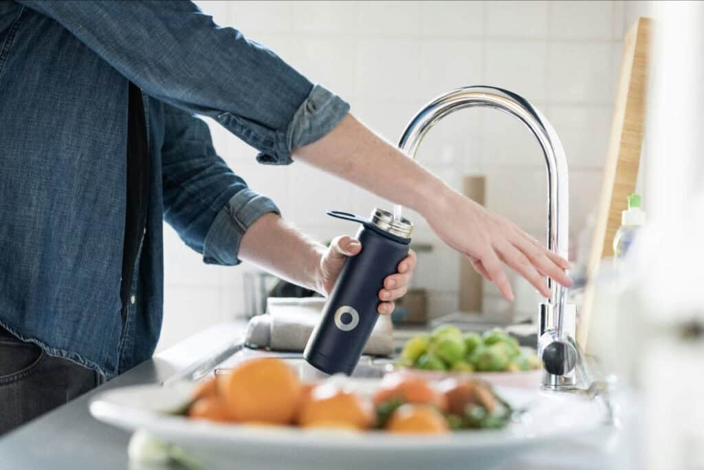 Person filling a water bottle at a kitchen sink, staying hydrated in the Oklahoma heat.