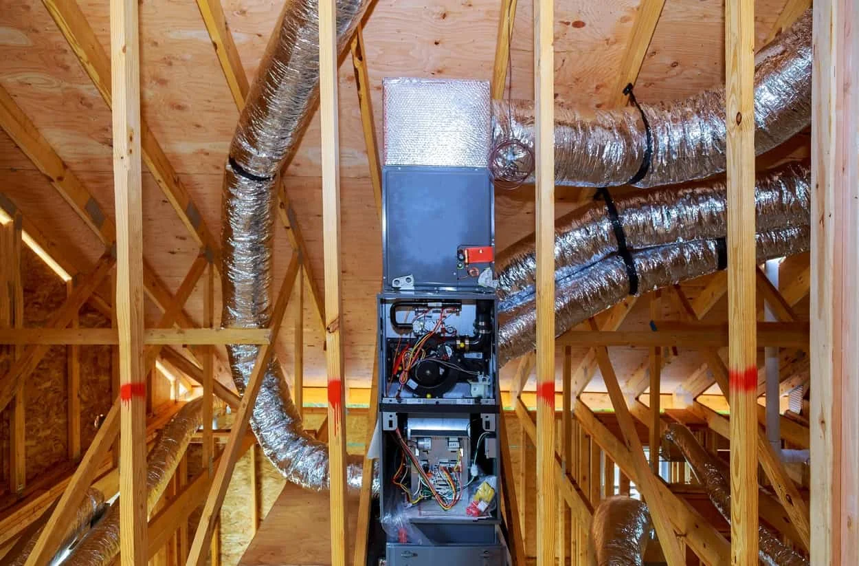 Ductwork installation by a local HVAC company in an attic, featuring an air handling unit and various ducts connected within the wooden framework.